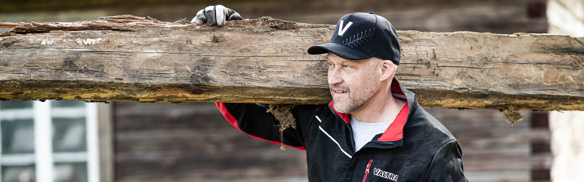 A farmer wearing Valtra Collection workwear carrying a large piece of wood