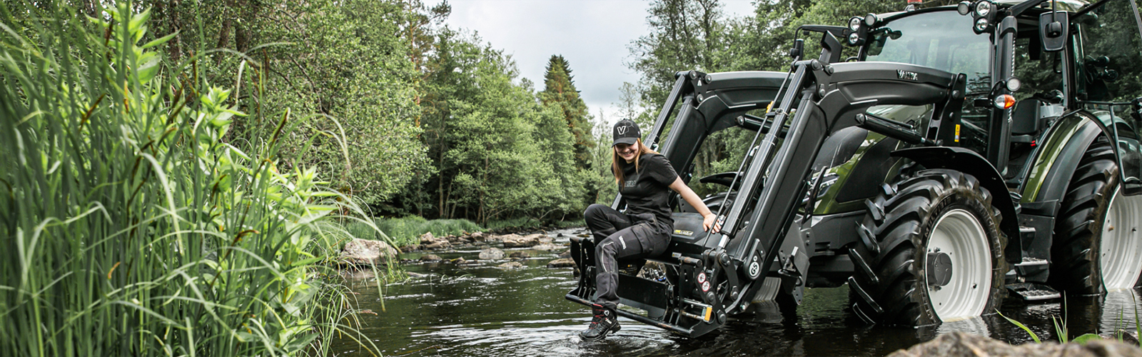 A Valtra farmer sits on their front loader while wearing Valtra Collection clothing
